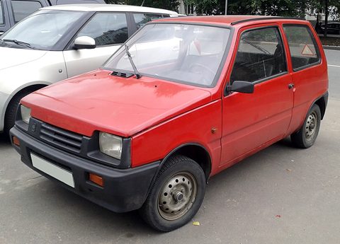 Red small three-door hatchback with black bumpers parked at a kerb beside a silver saloon.