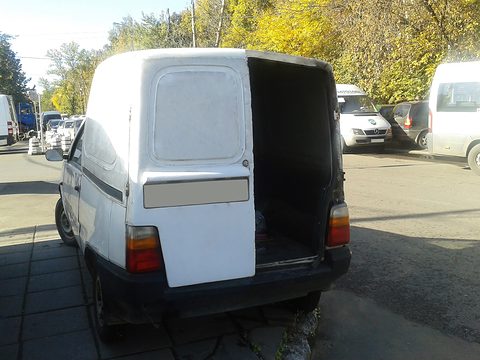 Rear of a white small van with tall boxy back and an open side-hinged rear door, parked in an autumn street. Opens a larger view