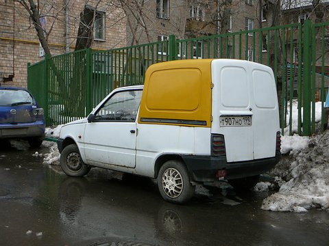 Rear quarter of a white small van with a yellow plastic upper body and twin rear doors, beside slushy snow. Opens a larger view