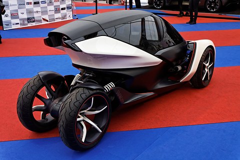 Rear of a white and black narrow tandem concept with exposed rear suspension on a red and blue carpet. Opens a larger view
