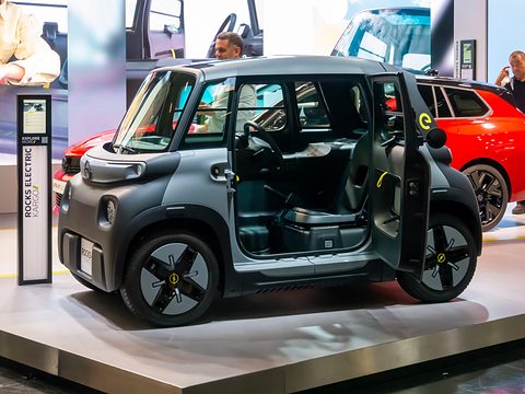 Grey cube-shaped car with both doors open on a raised stand, showing one seat and a load area where the passenger seat would be. Opens a larger view