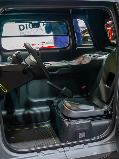 Cabin of a small car seen through the open door, with one black seat beside a flat grey load floor. Opens a larger view