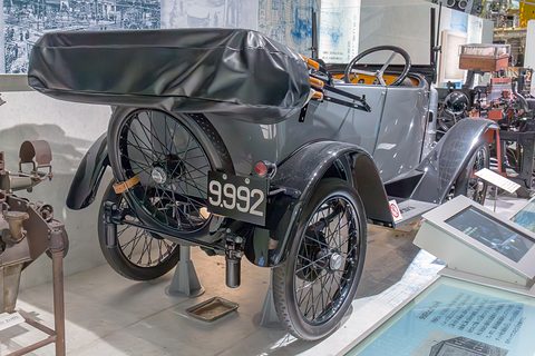 Rear view of a grey tourer showing a spare wire wheel, the folded hood and number plate 9992. Opens a larger view