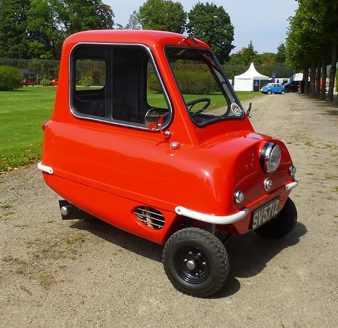 Tiny orange car on a gravel path in a park, seen from the front right. Opens a larger view