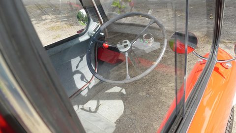 Steering wheel and seat seen through glass, gravel visible below. Opens a larger view