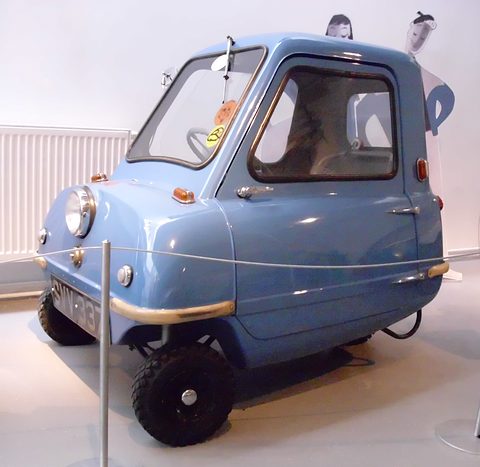 Tiny pale blue car with stickers in its window, seen from the front left behind a rope