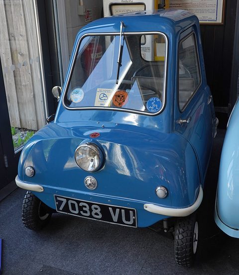 Tiny blue car seen from the front in a doorway, another car’s flank at right. Opens a larger view