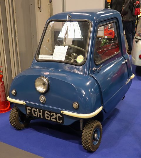 Tiny dark blue car seen from the front on a blue carpet, a card on its dashboard. Opens a larger view
