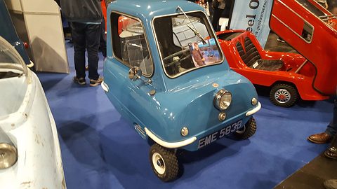 Tiny blue car on a blue show carpet with a photograph of a television presenter in its window