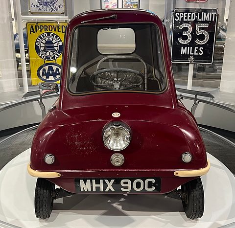 A dark red Peel P50 seen head-on on a museum turntable. Opens a larger view