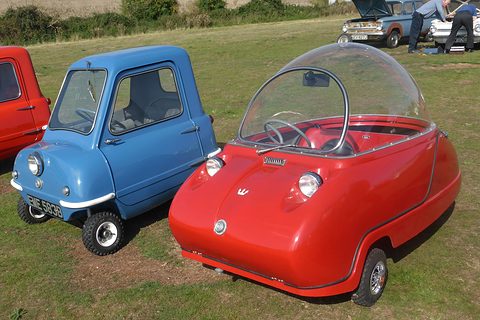 Red bubble car and a smaller blue single-door microcar side by side on grass.