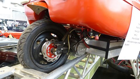 Close view of a small rear wheel with a disc brake under red bodywork. Opens a larger view