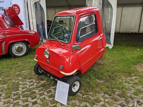 Tiny red car with a white information card on grass under a marquee. Opens a larger view