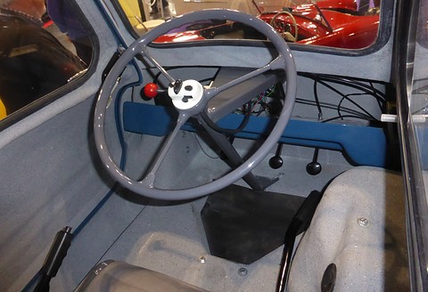 Grey steering wheel over a plain painted floor with a short gear lever and a seat