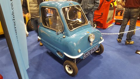 Tiny blue car on a blue carpet behind a chain, a club banner at left. Opens a larger view