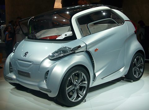 Silver short concept with an open rear door and multi-spoke wheels under cool stand lighting. Opens a larger view