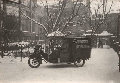 A three-wheeled delivery van lettered ‘Centralbadets Tvättinrättning’ parked on a snowy street. Opens a larger view