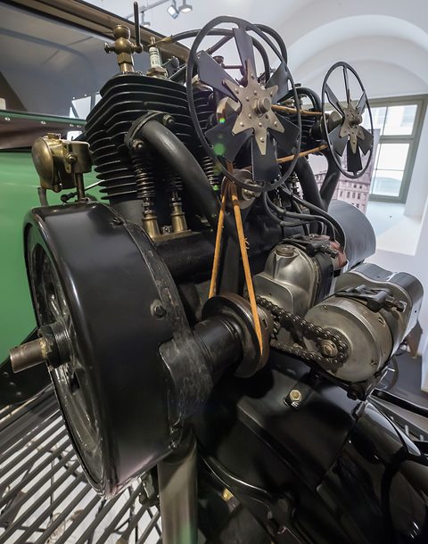 Close view of a finned engine with spoked fans and a drive chain above a front wheel. Opens a larger view