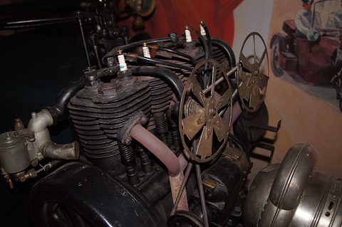 Close view of a finned four-cylinder engine with spark plugs and spoked fans. Opens a larger view