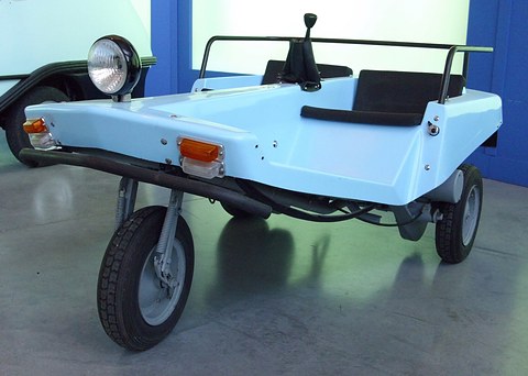 Low view of a pale blue three-wheeled tub with one sprung front wheel, a single headlamp and a black control stick.