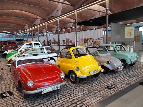 Red open two-seater at the front of a row of small cars, a yellow Isetta beside it, under a vaulted brick roof.