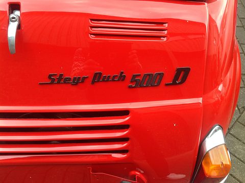 Close-up of black italic lettering above cooling louvres on a red engine lid, with an orange tail lamp at the right. Opens a larger view