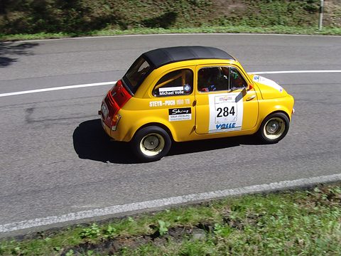 Yellow small saloon with black roof, red tail and ‘Steyr-Puch 650 TR’ lettering, seen from above on a mountain road.