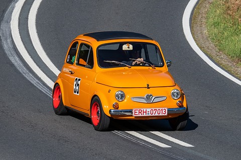 Orange small car with red wheels and number 35 cornering towards the camera on a curving road. Opens a larger view