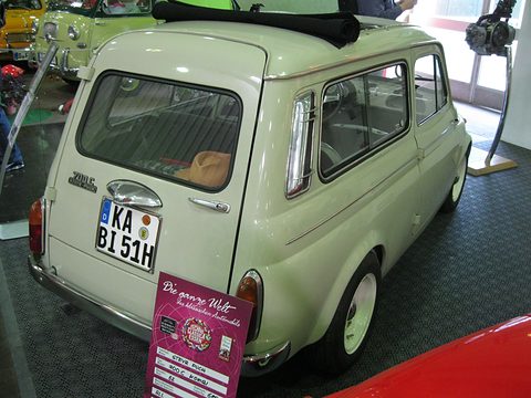 Rear of a cream estate car with folded fabric roof, chrome door handle, number plate and a pink show placard leaning against it. Opens a larger view