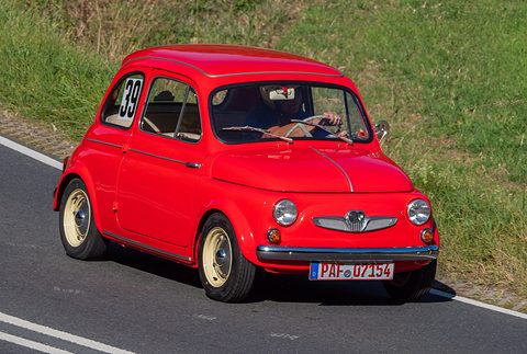 Bright red small car with cream wheels and number 39 in the side window, driving uphill past grass. Opens a larger view