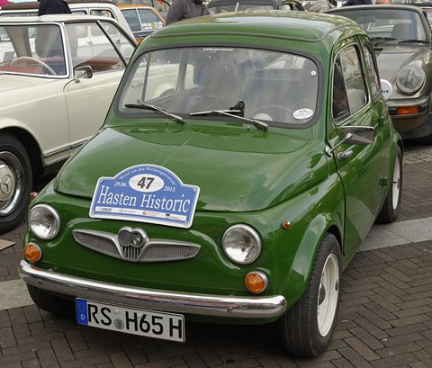 Dark green small saloon with chrome bumpers, Puch winged grille and a blue rally plaque on the bonnet, parked among classics. Opens a larger view