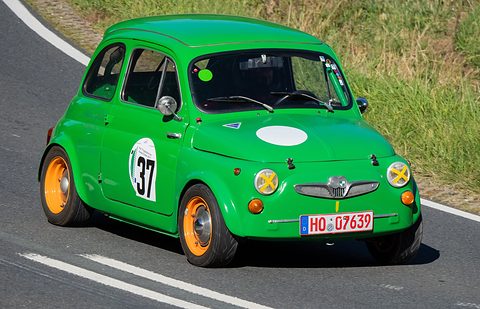 Bright green small car with number 37 and taped-over headlamps, cornering on a road edged with grass. Opens a larger view