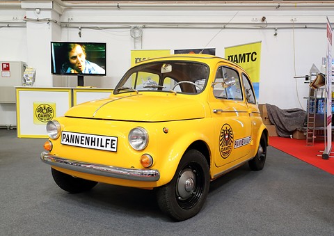 Yellow small saloon with ‘Pannenhilfe’ board across the nose and club eagle crest on the door, on a show stand.