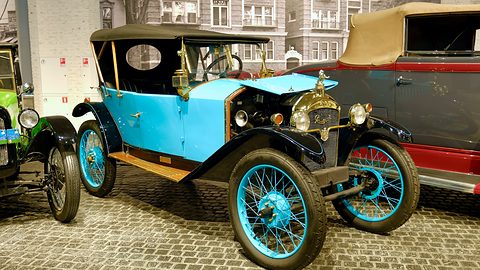 A turquoise open tourer with black wings and turquoise wire wheels on cobbles, other old cars around it. Opens a larger view