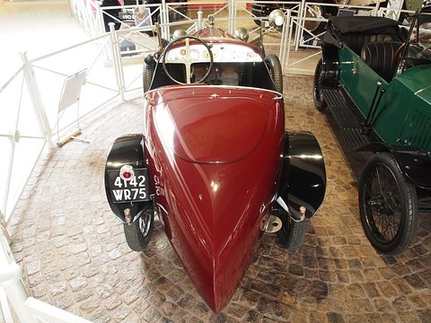 Rear view of a dark red car with a long tapering tail ending in a point, a plate 4142 WR 75 at its side. Opens a larger view