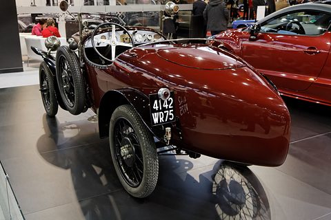 Rear quarter view of a dark red car with a long rounded tail and plate 4142 WR 75 on a grey stand. Opens a larger view
