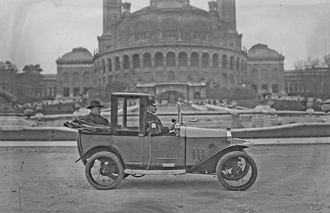 A narrow taxi with a tall enclosed passenger cab on open ground, the domed Trocadéro palace behind. Opens a larger view