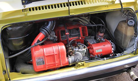 Open engine lid on a yellow car: a red-painted fan housing and air ducts filling the rear compartment.