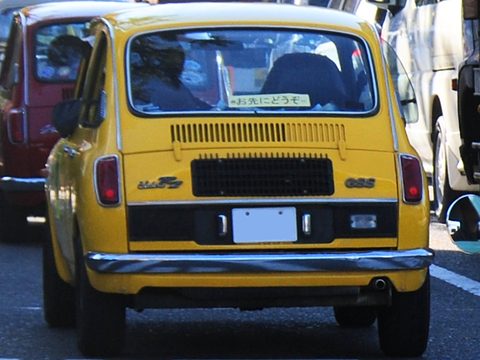 Yellow small saloon seen square from the rear: a black panel with louvres, round tail lamps and GSS lettering. Opens a larger view