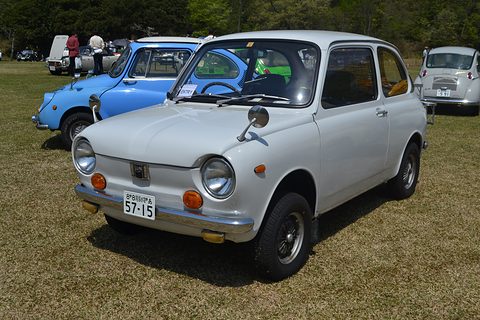 White small saloon on grass with round headlamps, a blue car parked behind. Opens a larger view