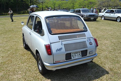 Rear view of a white small saloon with a louvred engine lid, on grass with other old cars behind. Opens a larger view