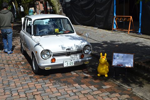 Silver small saloon on brick paving beside a yellow toy rabbit and a display board. Opens a larger view