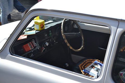 Through a silver car’s window: a wood-rimmed wheel, a black dashboard and a beaded seat cover. Opens a larger view