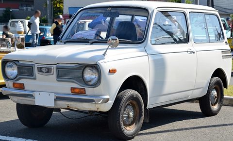 White small estate van with a long glazed rear, grille between round headlamps, visitors behind. Opens a larger view