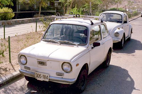White rounded small saloon with a roof rack, parked at the kerb with a white Subaru 360 behind. Opens a larger view
