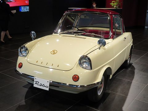 Cream small coupé with a maroon roof on a dark polished floor, an R360 plate on its bumper. Opens a larger view