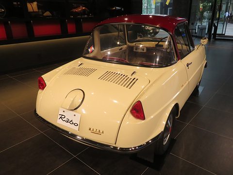 Rear three-quarter of a cream coupé with louvred lid and round filler, on a dark floor. Opens a larger view