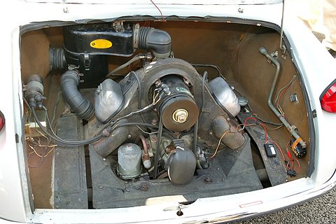 Open rear compartment of a white car showing a small V-twin engine with its fan housing and wiring.