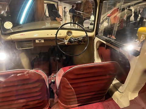Looking into a small coupé: red pleated seats, a thin two-spoke steering wheel and a cream dashboard. Opens a larger view