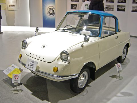 Cream small coupé with a turquoise roof on a grey floor, an R360 COUPE plate on its bumper. Opens a larger view
